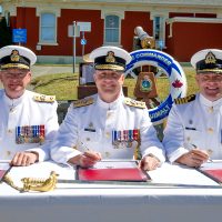 (Centre) Rear-Admiral Art McDonald, Commander Maritime Forces Pacific; former Base Commander Commodore Steve Waddell (left); and incoming Base Commander Captain (Navy) Jason Boyd (right), sign off on papers officially appointing Capt(N) Boyd to his new post during a Change of Command Ceremony at Museum Square, June 22.