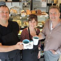 From left: Kindness Ambassador Greg Hind is joined by A Kinder Cup owners Chief Petty Officer First Class (Retired) Marc Dufort and Kim Dufort as they raise a toast to their new coffee shop at Admirals Walk Plaza. Photo by Peter Mallett, Lookout