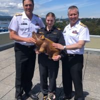 Commodore Angus Topshee (left), Commander Canadian Fleet Pacific; Lieutenant(N) Holly Swallow (centre) of Her Majesty’s New Zealand Ship Te Kaha, and Vice-Admiral Art McDonald, Commander Royal Canadian Navy, hold Te Kaha’s wooden pig mascot. The mascot was snuck off the ship 20 years ago by the Admiral as a friendly prank.