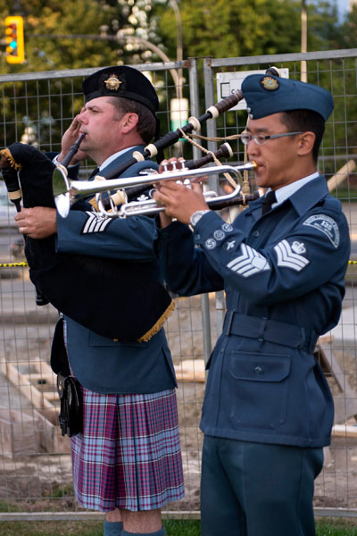 A trumpeter from the Albert Head Cadet Band plays the Last Post while a member of the 443 Military Helicopter Squadron Pipe and Drum Band salutes at the 24th Annual Canadian Peacekeeping Memorial Day Parade. Photo by LS Ogle Henry, MARPAC Imaging Services