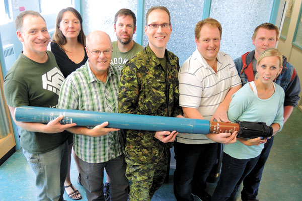 Civilian ammunition technicians in training (Left) Ed Cawley, Michelle Chowns, Tervor Marcotte, Scott Mathieson, Alfred Nelson and Kala Chaulk display a 100 mm Shield Practice Rocket at Rocky Point Ammunition Depot. They are joined by Rocky Point Commanding Officer Maj Jean-Luc Rioux (fourth from right) and Material Processing Officer Makr Field (third from left). Photo by Peter Mallett, Lookout