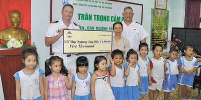 Commander Clive Butler (left), Commanding Officer of HMCS Vancouver, and Chief Petty Officer First Class Tim Blonde (right), Coxswain, present a donation of $5,000 on behalf of the Boomer’s Legacy Fund to Dang Thi Huong (center), Director of SOS Children’s Villages.