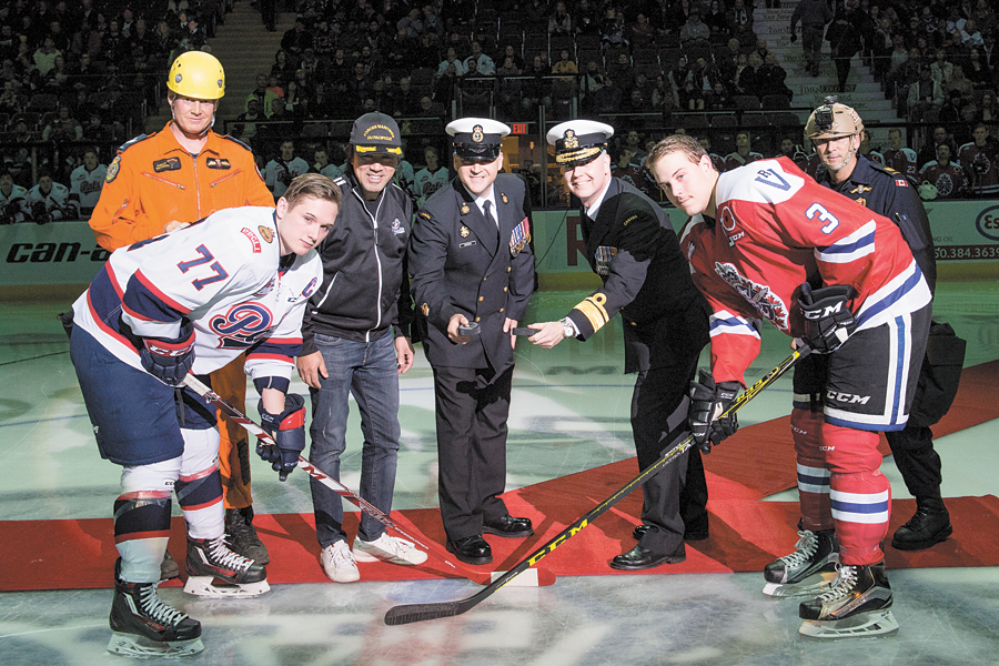 Rear Admiral Art McDonald, Commander Maritime Forces Pacific, and Chief Petty Officer First Class Gilles Grégoire, Formation Chief Petty Officer, ready for the ceremonial puck drop between Adam Brooks, Captain of the Regina Pats, and Ryan Gagnon, Captain of the Victoria Royals, at centre ice.