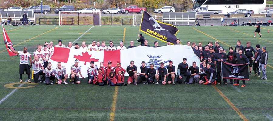 Touch football teams representing HMCS Calgary, dressed in white (left), and HMCS Ottawa, dressed in black (right) gather for a group photograph ahead of their pre-Grey Cup game. Photo by LS Ogle Henry, MARPAC Imaging Services