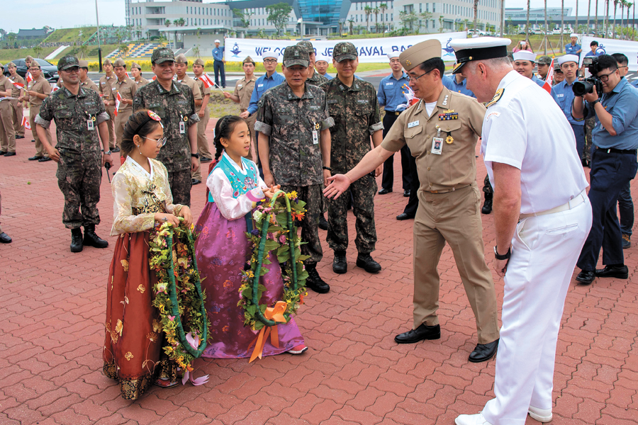 Commodore J.B. Zwick, Commander of Canadian Fleet Pacific, is presented a flower necklace by two South Korean children, during HMCS Winnipeg’s visit to Jeju Naval Base, South Korea, June 22. Photo by Cpl Carbe Orellana, MARPAC Imaging Services