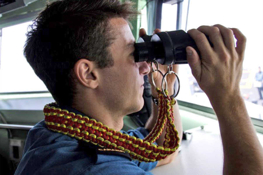 Ordinary Seaman Olivier Gingras uses binoculars with a decorative strap knotted by the Deck Department. Photo by Royal Canadian Navy Public Affairs