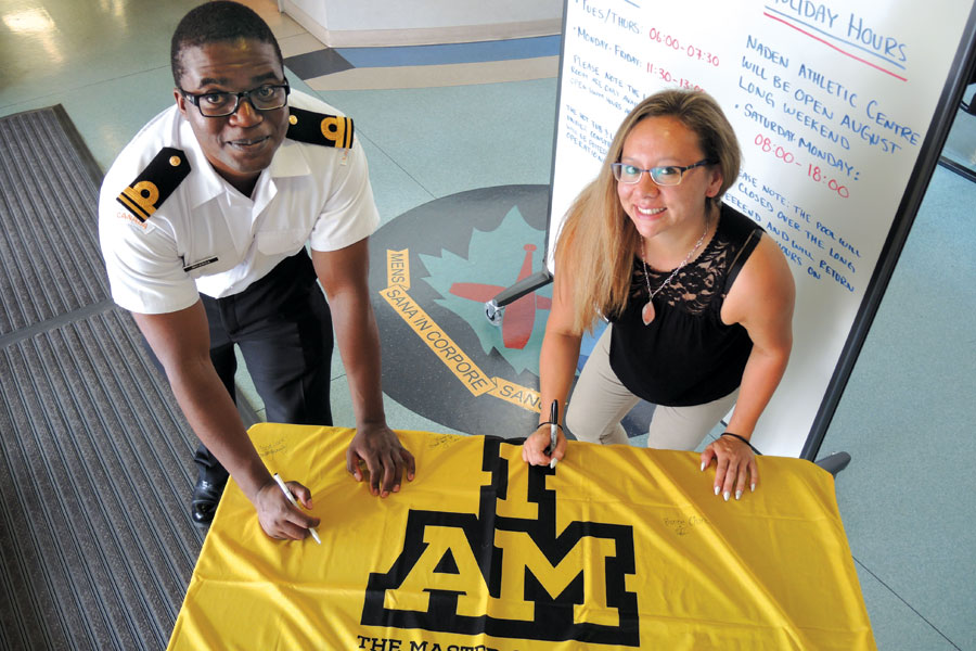 SLt Tawonga Mkanda (left), a Deputy Base Personnel Services Officer at Base Administration, and Amy Lee, Administrative Assistant at Base Administration, sign their names and words of encouragement on the Invictus Games flag at the Naden Athletic Centre. Photo by Peter Mallett, Lookout Newspaper