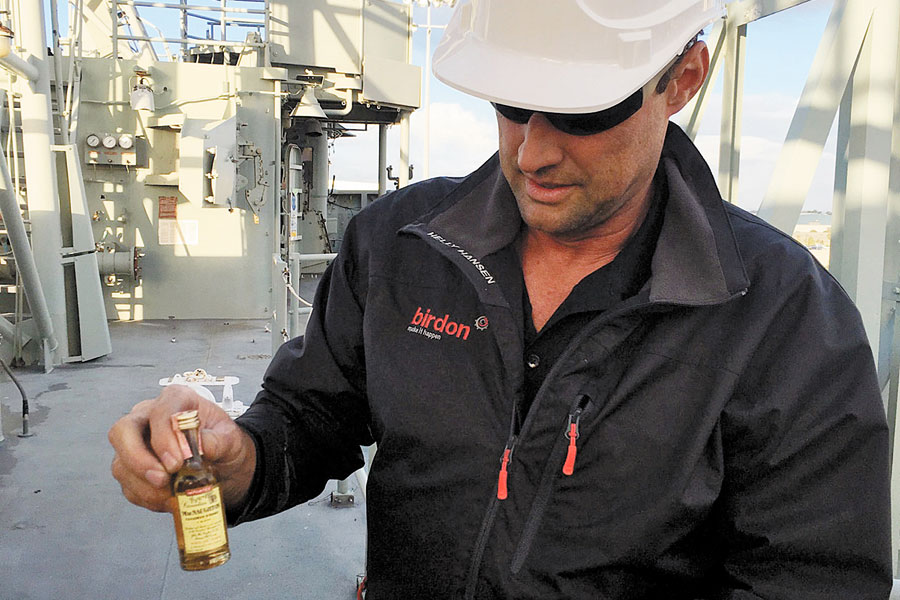 An employee working on the scrapping of HMAS Sydney removes the bottle of whisky from its package of insulation tape after it was recovered from the main mast.
