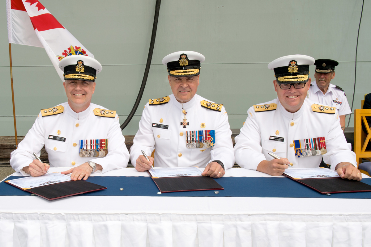 From the left: Rear-Admiral Art McDonald, the outgoing Commander of Maritime Forces Pacific and Command Joint Task Force (Pacific), Vice-Admiral Ron Lloyd, Commander of the Royal Canadian Navy, and Rear-Admiral Bob Auchterlonie sign the Change of Command certificates with HMCS Calgary behind them on June 22. Photo by LS David Gariepy, MARPAC Imaging Services