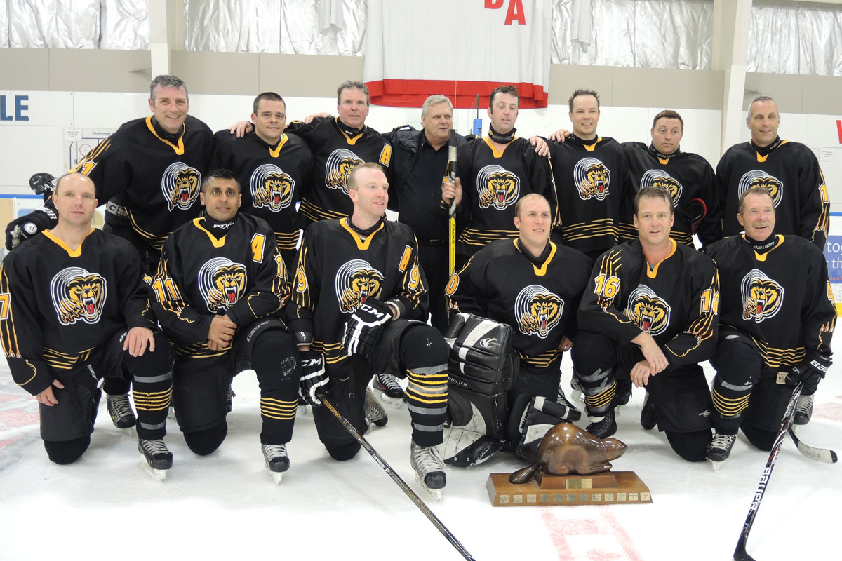 The Esquimalt Fire Bear gather for a team photo after their gold medal win. Right: Fire Bears team captain Josh Peterson of Esquimalt Fire and Rescue raises the Beaver Cup trophy over his head in celebration of their win. Inset below: Blues guitarist Jesse Roper and member of the RPOps Thrashers belts out a rendition of O Canada on his guitar during the Beaver Cup opening ceremony at Wurtele Arena. Photo by Peter Mallett, Lookout