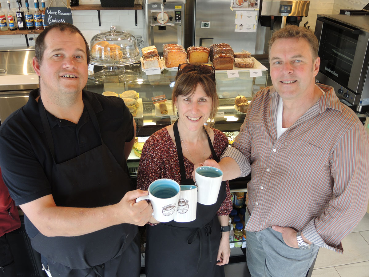 From left: Kindness Ambassador Greg Hind is joined by A Kinder Cup owners Chief Petty Officer First Class (Retired) Marc Dufort and Kim Dufort as they raise a toast to their new coffee shop at Admirals Walk Plaza. Photo by Peter Mallett, Lookout
