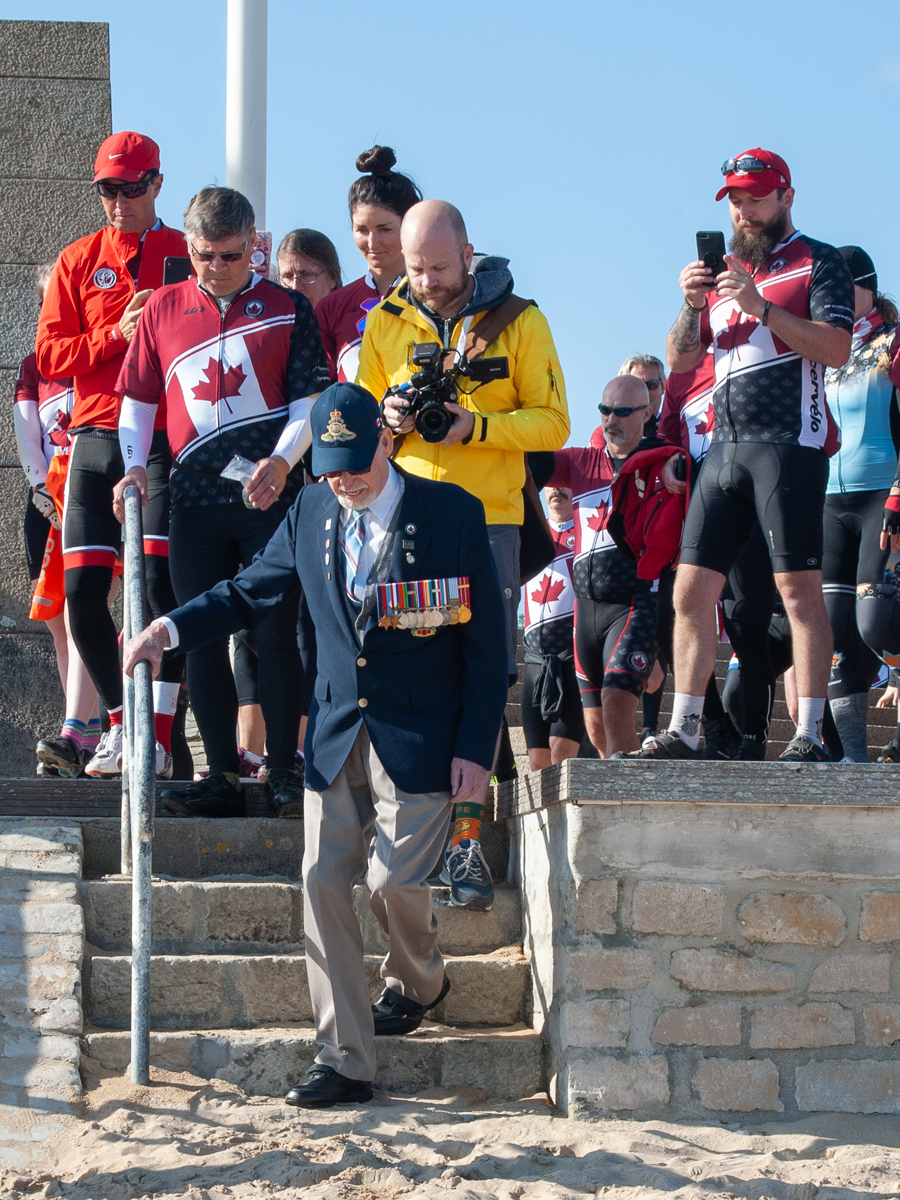 Second World War veteran Russ Kaye is joined by Battlefield Bike Ride cyclists as he makes his way down the steps to set foot on Juno Beach for the first time in 75 years. Photo by John W. Penner/John’s Photography