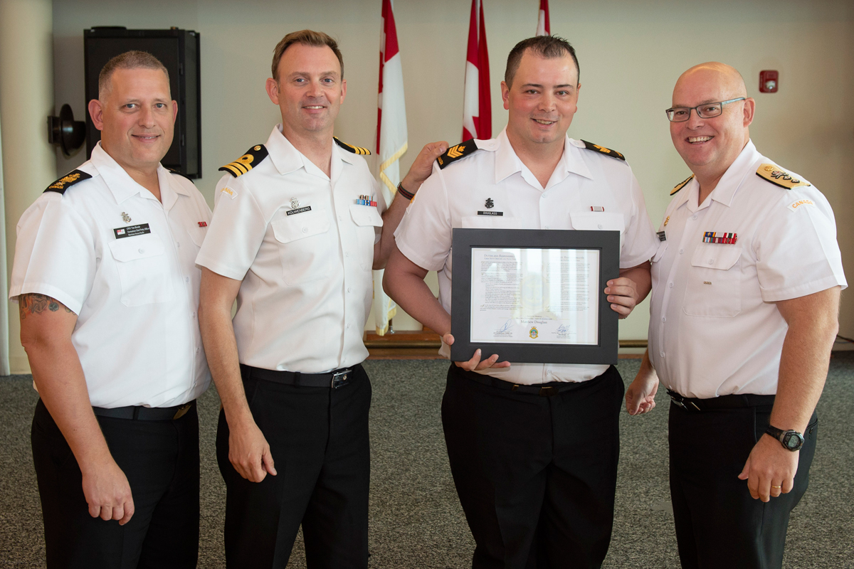 Petty Officer Second Class Matthew Douglass is introduced to the Chiefs’ and Petty Officers’ Mess and presented with the certificate of Duties and Responsibilities by Chief Petty Officer First Class Tim Blonde, MARPAC Formation Chief Petty Officer (left), Commander Jonathan Kouwenberg, Commanding Officer of HMCS Calgary, and Rear-Admiral Bob Auchterlonie, Commander MARPAC.