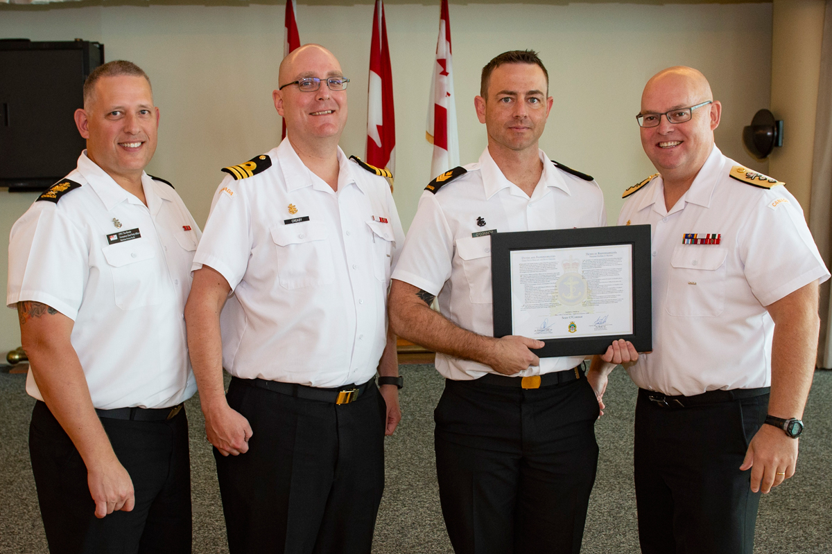 Petty Officer Second Class Sean O’Conner is introduced to the Chiefs’ and Petty Officers’ Mess and presented with the certificate of Duties and Responsibilities by Chief Petty Officer First Class Tim Blonde, MARPAC Formation Chief Petty Officer (left), Commander Landon Creasy, Commanding Officer of HMCS Regina, and Rear-Admiral Bob Auchterlonie, Commander MARPAC.