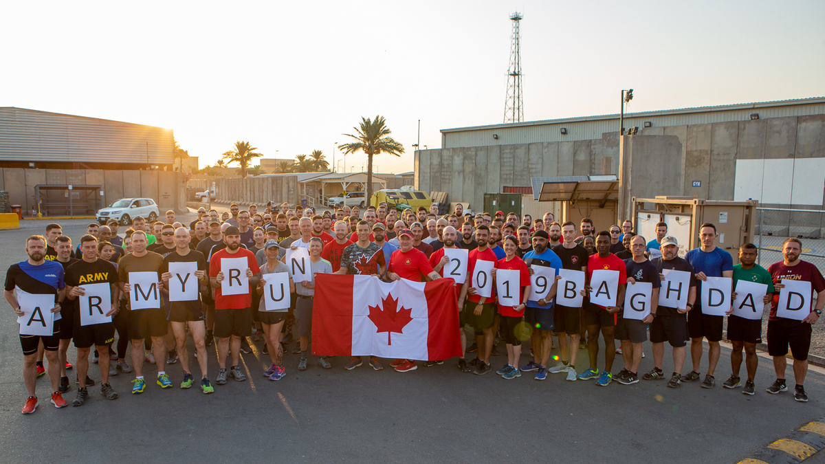 A group of Canadian Armed Forces personnel hold up a Canadian flag after participating in an Army Run at Union III military installation in Baghdad. Photo credit DND