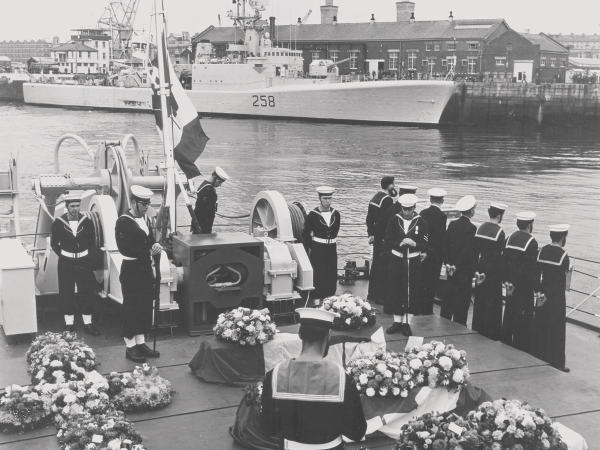 Funeral service for the nine deceased crew members of HMCS Kootenay with the burnt and damaged ship in the background at Devonport, UK, Oct. 27, 1969. The ceremony was held on board HMCS Saguenay, a fellow ship that had served alongside Kootenay in the naval exercise.