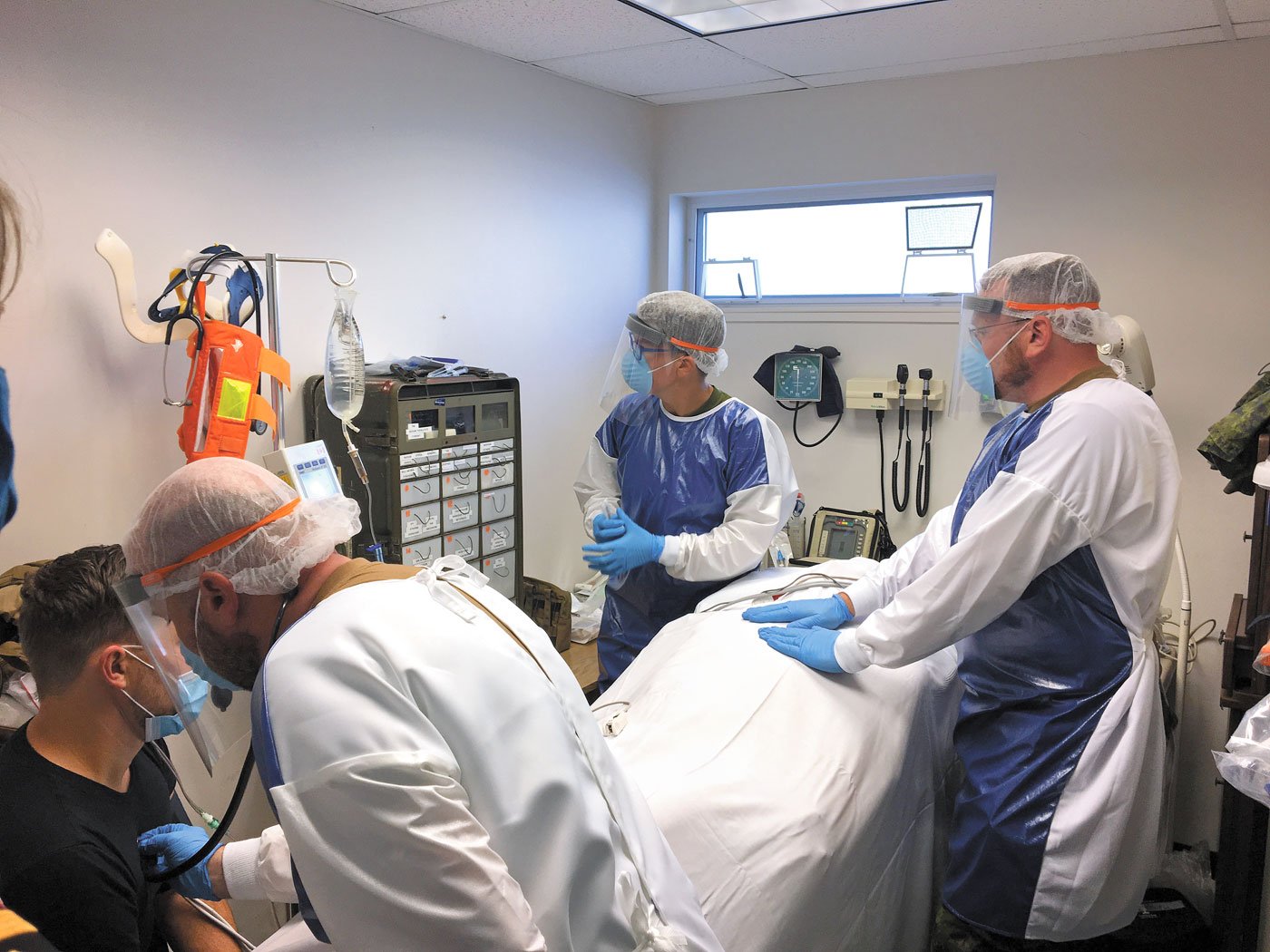 Capt Brown and his team, MCpl Cape and Cpl Smith, assess a patient with possible SARS-CoV-2 symptoms. The team is wearing full Personal Protective Equipment. The combination of a live role player and simulated casualty (mannequin) was used for the training scenarios. The team questioned and examined the role player and then performed required interventions on the mannequin.