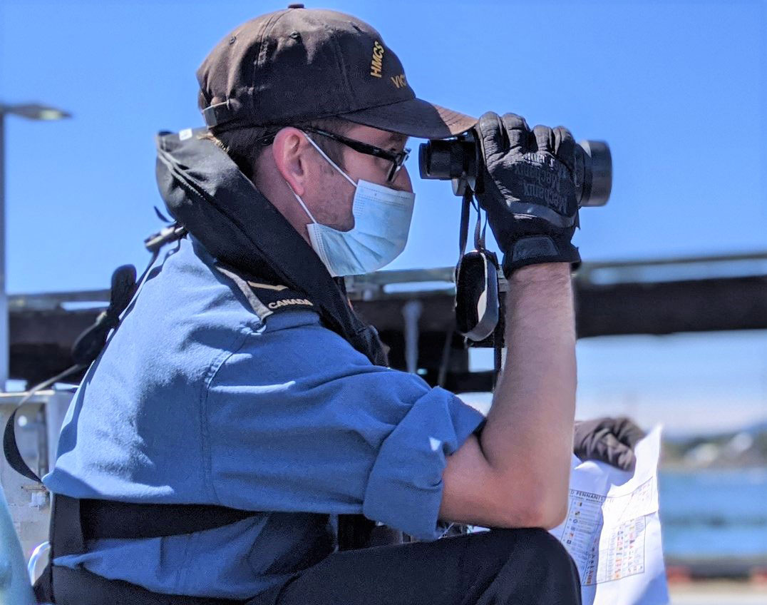 Sailor Second Class Nick Reicker uses binoculars to scout for and identify nautical flags during a recent training exercise off the jetty of HMCS Malahat.