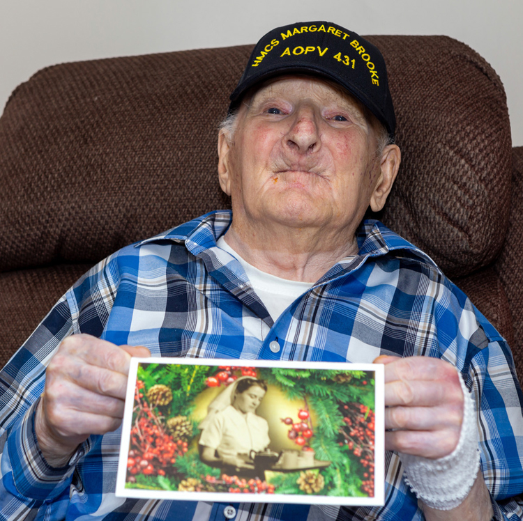 Howard Lake, 102, from Grand Bank, NFLD, reads a card sent to him by Cdr Michele Tessier while wearing his new HMCS Margaret Brooke baseball hat. Lake served in the Second World War and, along with  nursing sister Margaret Brooke, survived a torpedo attack while transiting aboard passenger ferry SS Caribou from Nova Scotia to Newfoundland in 1942. Brooke was later honoured for her heroic effort to save a fellow nursing sister. The Arctic and Offshore Patrol Vessels are named for courageous Canadians such as Brooke. Photo credit: Carl Rose
