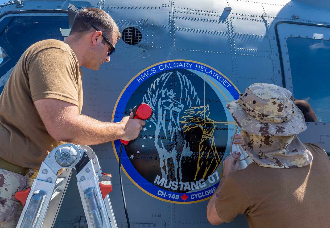 Master Corporal Andrew Finnigan, an Aviation Systems Technician, and Corporal Brendan Wales, an Aircraft Structures Technician, apply the detachment’s operational decal to the CH-148 Cyclone. Photos by Cpl Lynette Ai Dang, Imagery Technician