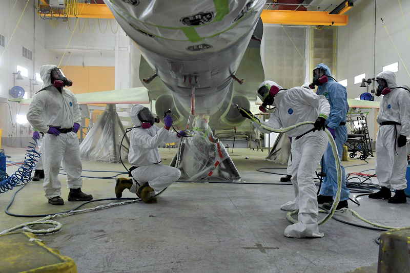 Corporal Frederick Schinck (second from the left) and Aviator James Schneider (centre, third from the right) apply the first coat of NATO standard gray to the underbelly of a fighter jet at Aerospace and Telecommunications Engineering Support Squadron. Photos by Stacey Payne, ATESS