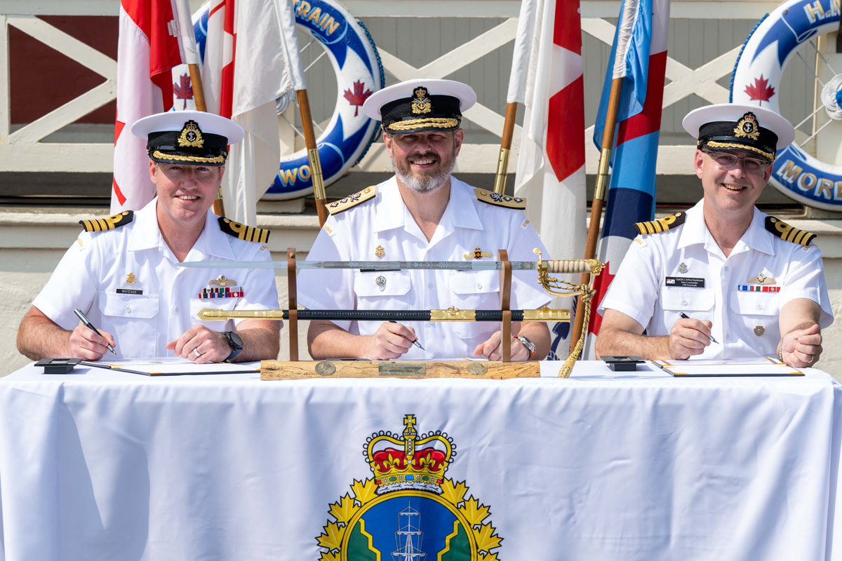 Left to right at the table, Incoming Base Commander Captain (Navy) Kevin Whiteside, CD, Reviewing Officer Rear Admiral Christopher Robinson, CD, and Outgoing Base Commander Jeff Hutchinson, sign the transfer of command papers at the Change of Command Ceremony held at the Base Museum Bldg N-27, Canadian Forces Base Esquimalt, On July 7th, 2023.<br />
Photo: Cpl Tristan Walach, MARPAC Imaging Services, Esquimalt