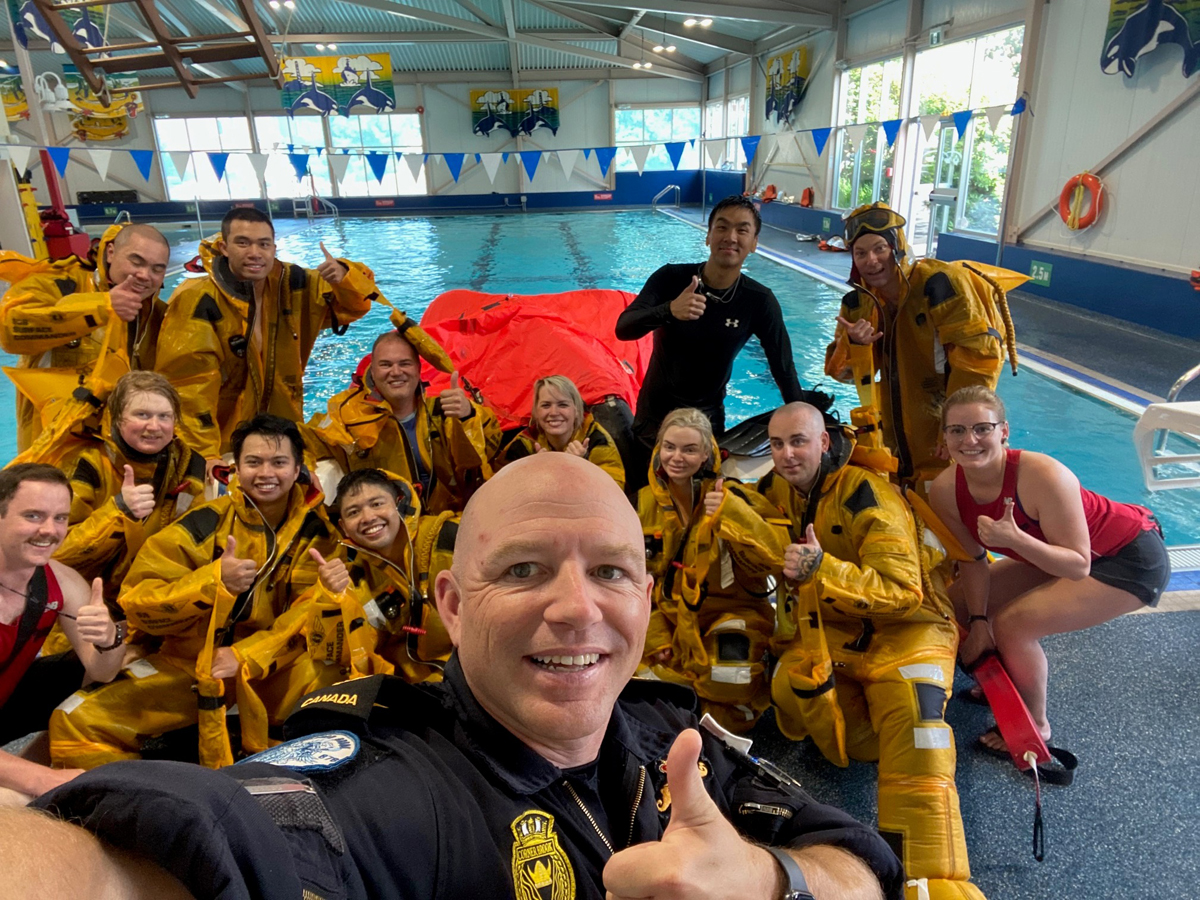 Le Capitaine de frégate Eric Isabelle, commandant du NCSM Corner Brook, prend un selfie avec les membres de l'équipe pendant le cours de recyclage sur l'évacuation.