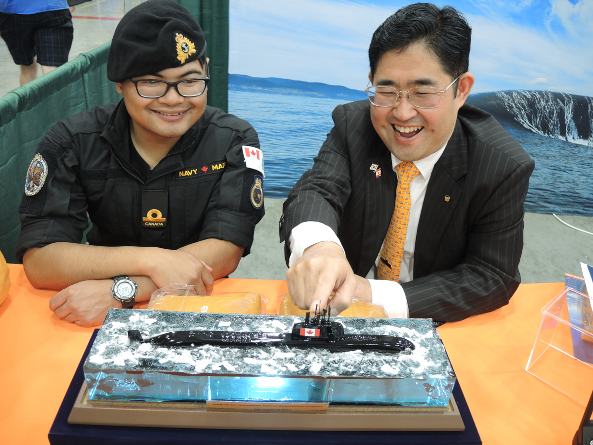 L’Enseigne de vaisseau de deuxième classe Chris Mejia, du NCSM Regina, examine la maquette d’un sous-marin en compagnie de Vincent Kim, directeur général de l’équipe de marketing outre-mer pour la marine et les navires de Hanwha Ocean.