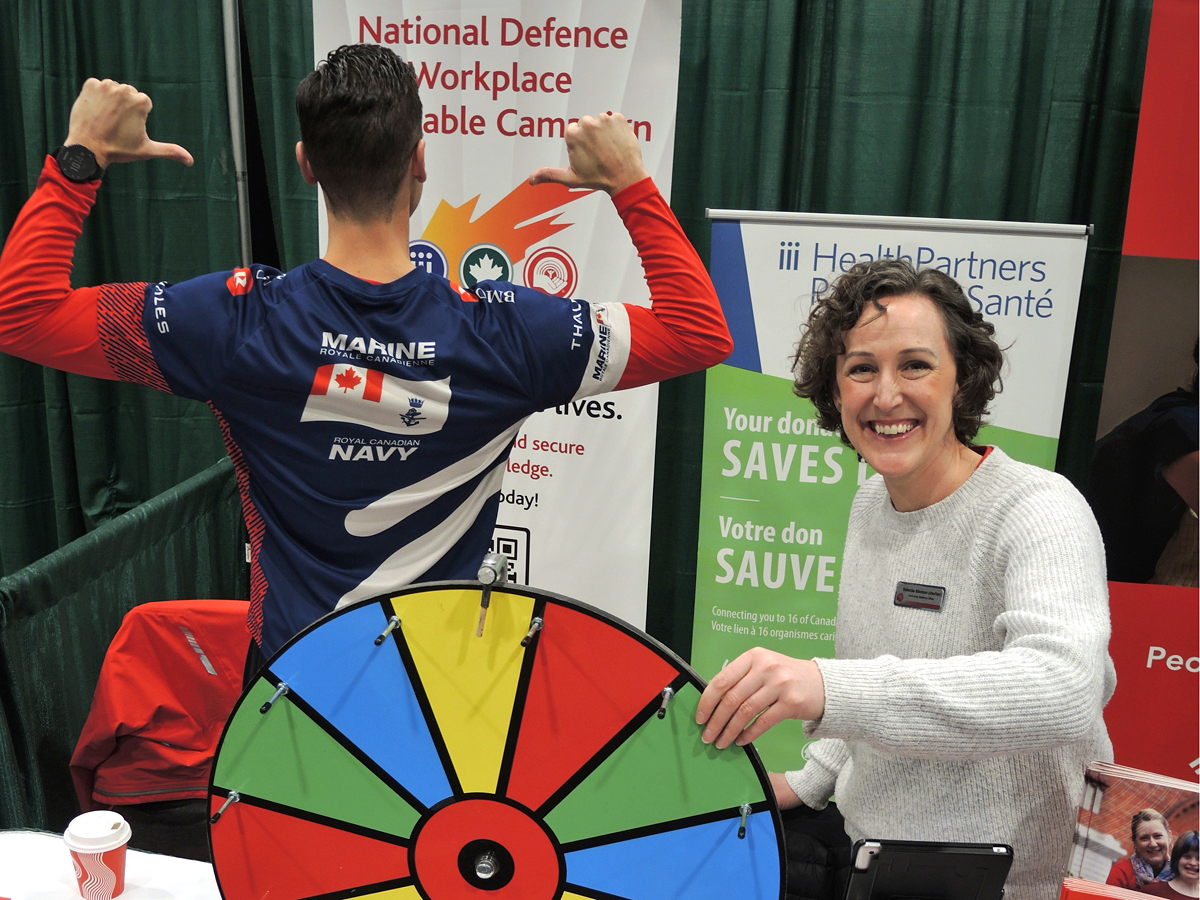 Matt Carlson, Projects Officer for Base Public Affairs, celebrates the achievements of the National Defence Workplace Charitable Campaign (NDWCC) while Rebecka Ibbotson of United Way of Southern Vancouver Island spins the prize wheel at the NDWCC booth.
